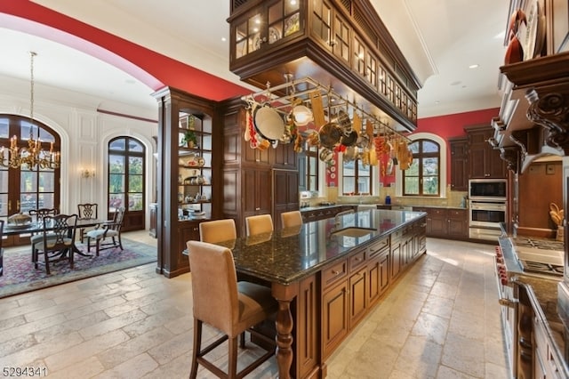 kitchen with dark stone counters, crown molding, an inviting chandelier, a center island, and appliances with stainless steel finishes