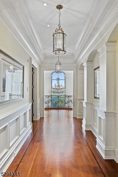 hall featuring ornate columns, hardwood / wood-style floors, ornamental molding, and a chandelier