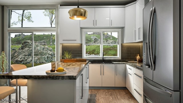 kitchen featuring hanging light fixtures, tasteful backsplash, hardwood / wood-style flooring, stainless steel fridge, and sink