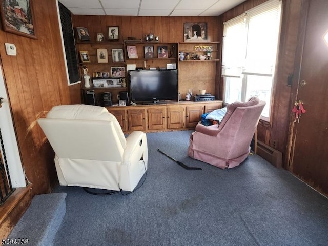 carpeted living room featuring baseboard heating, a drop ceiling, and wood walls