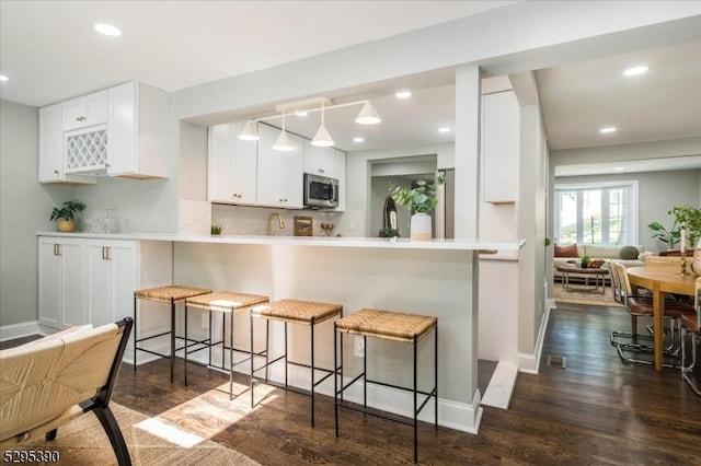 kitchen with kitchen peninsula, dark hardwood / wood-style floors, a kitchen breakfast bar, and white cabinetry