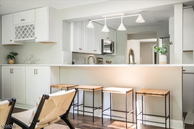 kitchen with dark hardwood / wood-style flooring, white cabinets, a breakfast bar, and kitchen peninsula