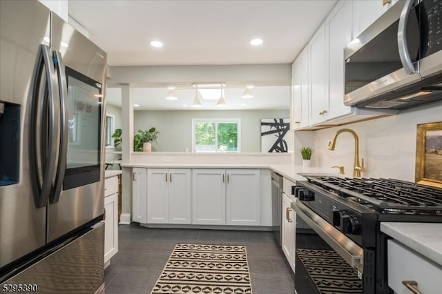 kitchen featuring appliances with stainless steel finishes, white cabinetry, dark tile patterned floors, and kitchen peninsula