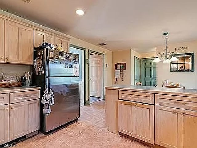 kitchen with black refrigerator, light brown cabinets, decorative light fixtures, and a notable chandelier