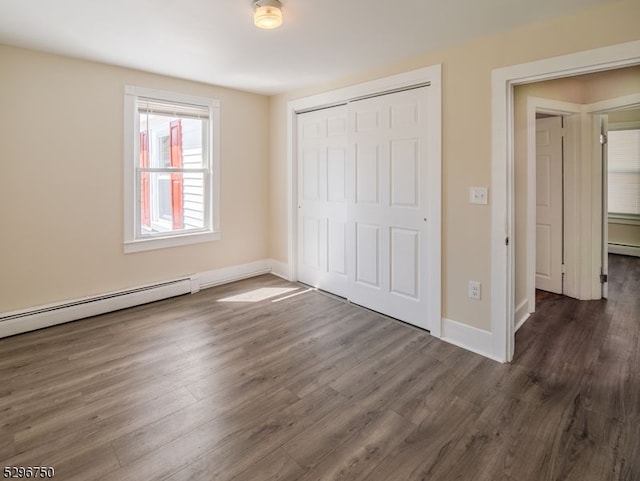 unfurnished bedroom with a closet, dark hardwood / wood-style floors, and a baseboard heating unit