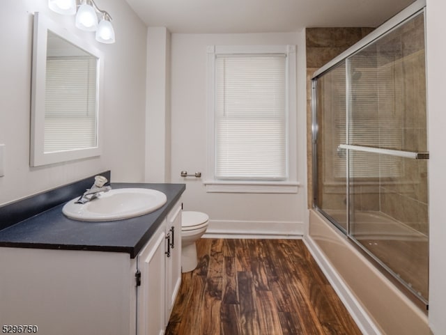 full bathroom featuring vanity, bath / shower combo with glass door, hardwood / wood-style flooring, and toilet