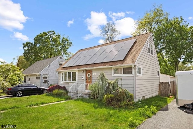 view of front facade with roof mounted solar panels, a front yard, and roof with shingles