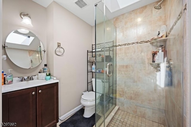 bathroom featuring toilet, a skylight, vanity, a shower stall, and baseboards