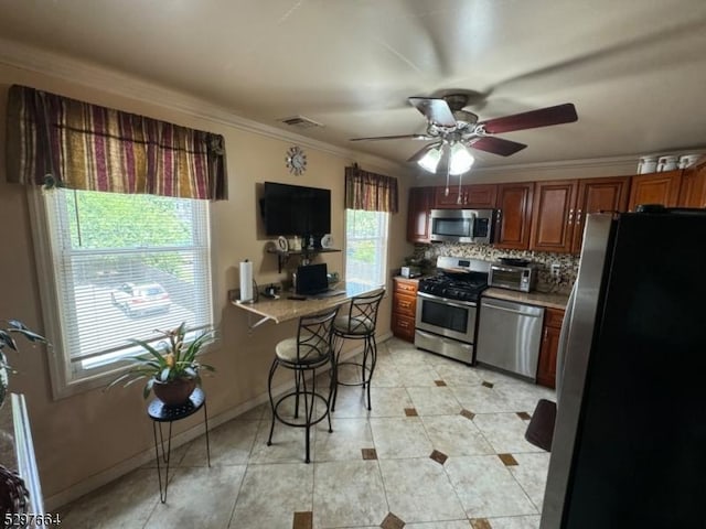 kitchen with light tile patterned floors, crown molding, ceiling fan, stainless steel appliances, and decorative backsplash