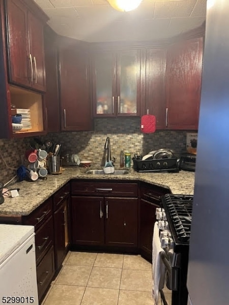 kitchen with gas range, backsplash, sink, and light tile patterned flooring