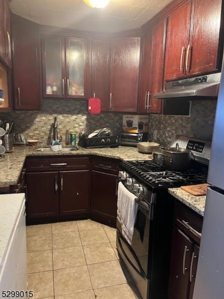 kitchen with tasteful backsplash, sink, light tile patterned floors, gas range, and light stone countertops