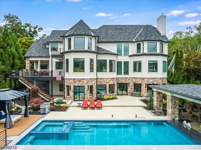 back of property with stucco siding, a pool with connected hot tub, stairway, and a patio