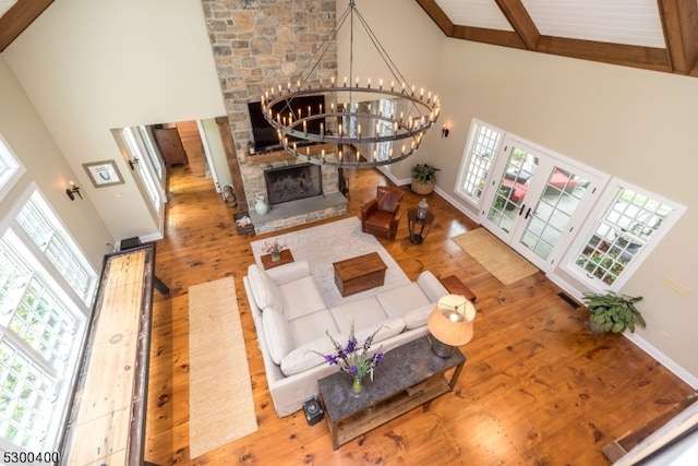 living room with a stone fireplace, beamed ceiling, hardwood / wood-style flooring, high vaulted ceiling, and plenty of natural light