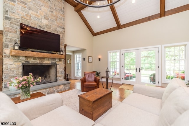 living room featuring hardwood / wood-style flooring, high vaulted ceiling, beam ceiling, french doors, and a stone fireplace