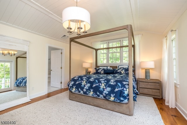 bedroom with an inviting chandelier, ensuite bathroom, wood-type flooring, and vaulted ceiling