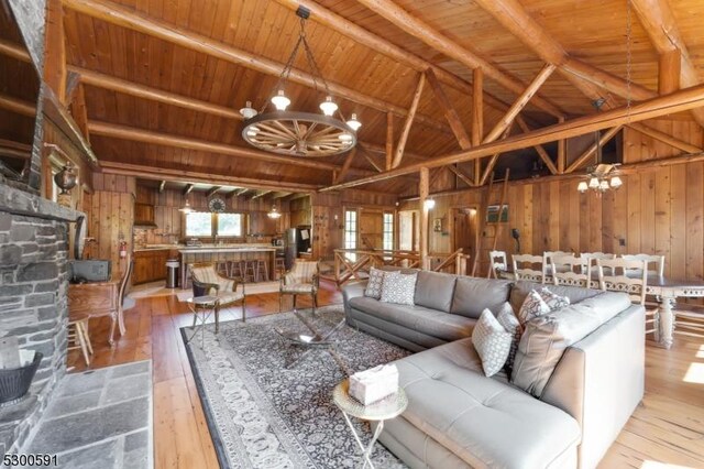 living room with vaulted ceiling with beams, wood ceiling, an inviting chandelier, light wood-type flooring, and wood walls