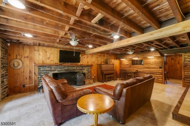 living room with a stone fireplace, ceiling fan, light tile patterned floors, and beam ceiling