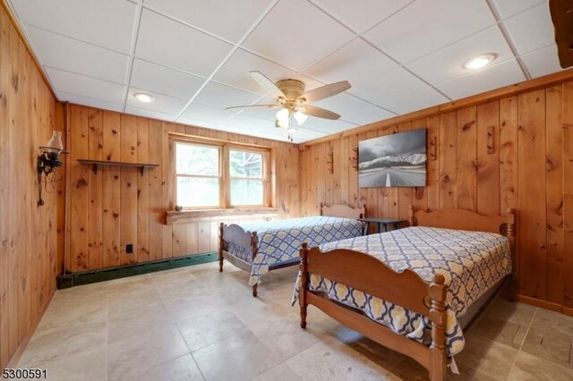 tiled bedroom with wooden walls, a baseboard heating unit, ceiling fan, and a paneled ceiling