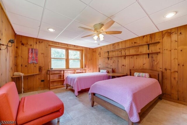 tiled bedroom featuring wooden walls, ceiling fan, and a paneled ceiling