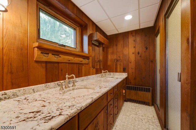 bathroom featuring a paneled ceiling, vanity, radiator, and wooden walls