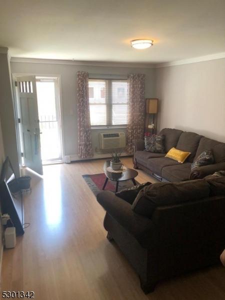 living room featuring a wall mounted air conditioner, ornamental molding, and hardwood / wood-style floors