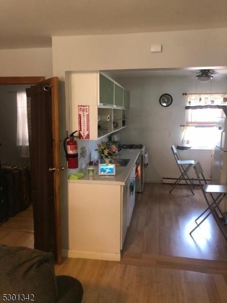 kitchen with white range oven, light wood-type flooring, a baseboard heating unit, and white cabinets