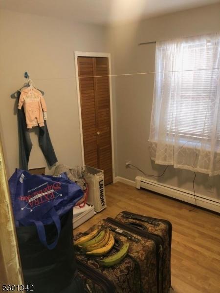 bedroom with a closet, a baseboard heating unit, and light wood-type flooring