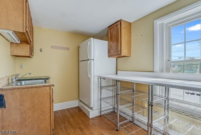 kitchen featuring a sink, freestanding refrigerator, wood finished floors, baseboards, and light countertops