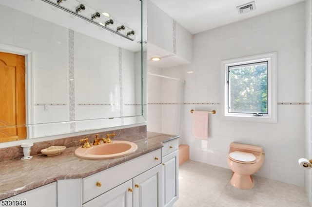 bathroom with tile patterned floors, toilet, vanity, tile walls, and walk in shower