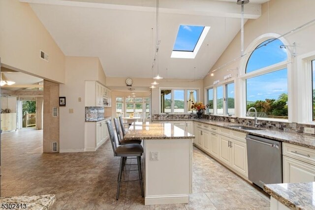 kitchen with a skylight, light stone counters, stainless steel dishwasher, sink, and high vaulted ceiling