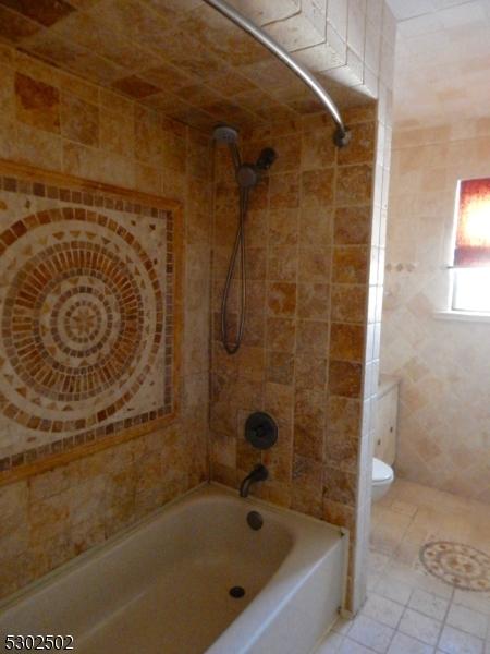 bathroom with tile patterned floors, toilet, tiled shower / bath combo, and tile walls