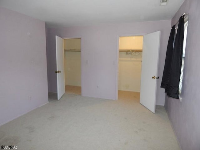 unfurnished bedroom with multiple windows, a walk in closet, light carpet, and a closet