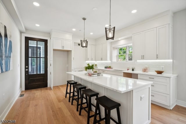 kitchen featuring light hardwood / wood-style floors, white cabinetry, decorative light fixtures, a kitchen island, and decorative backsplash