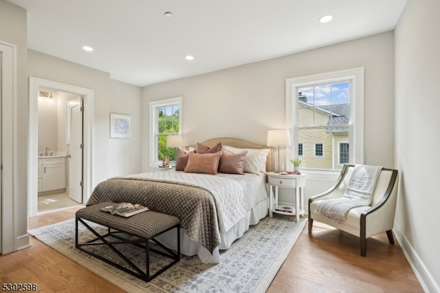 bedroom with light hardwood / wood-style floors, multiple windows, sink, and connected bathroom