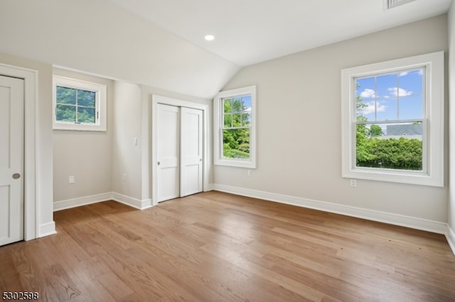 unfurnished bedroom featuring light wood-type flooring, multiple windows, and vaulted ceiling