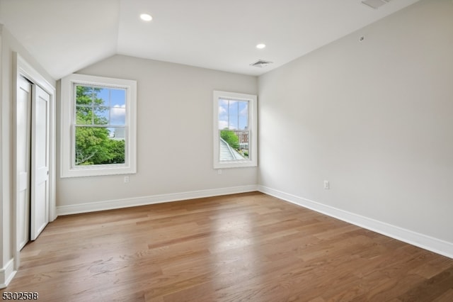 unfurnished bedroom with multiple windows, light hardwood / wood-style flooring, and lofted ceiling