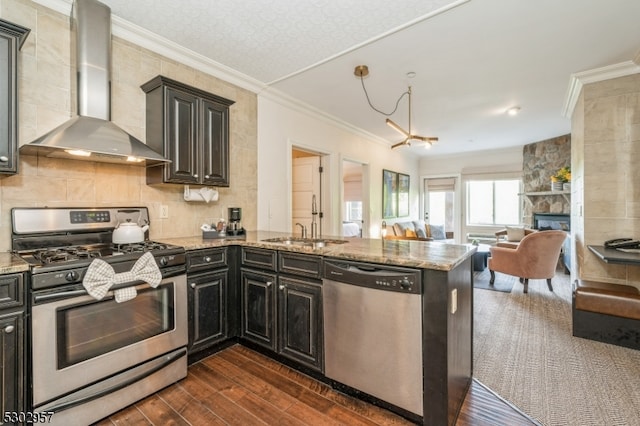 kitchen with a fireplace, wall chimney range hood, stainless steel appliances, light stone counters, and dark wood-type flooring