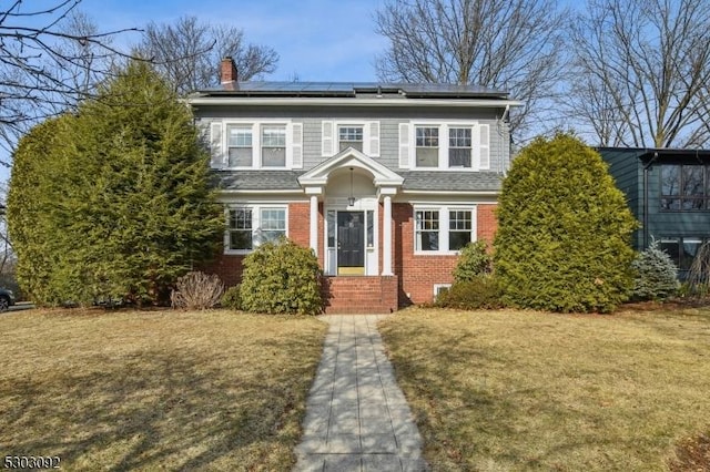 view of front of property featuring solar panels, brick siding, a front lawn, and a chimney