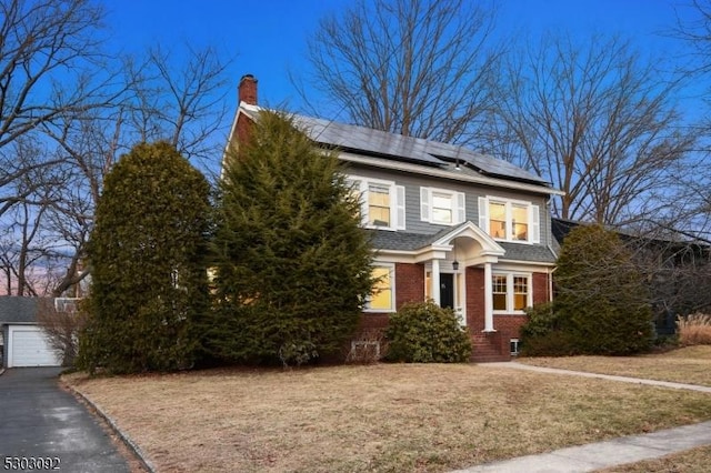 view of front of house featuring a front yard, a chimney, solar panels, and brick siding