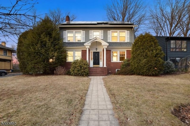 traditional home featuring a chimney, a front lawn, solar panels, and brick siding