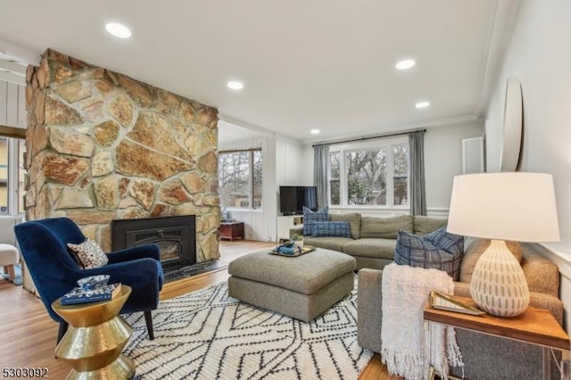 living area featuring ornamental molding, a stone fireplace, light wood finished floors, and recessed lighting