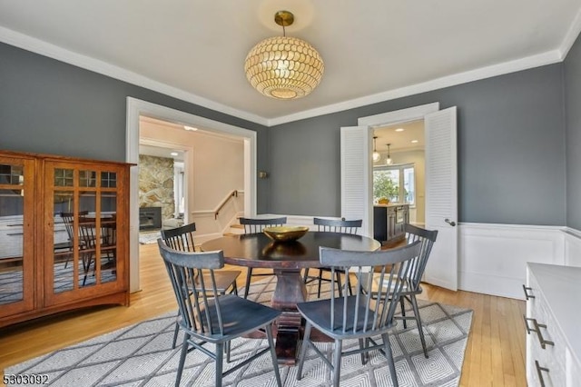 dining space with ornamental molding, light wood-type flooring, and wainscoting