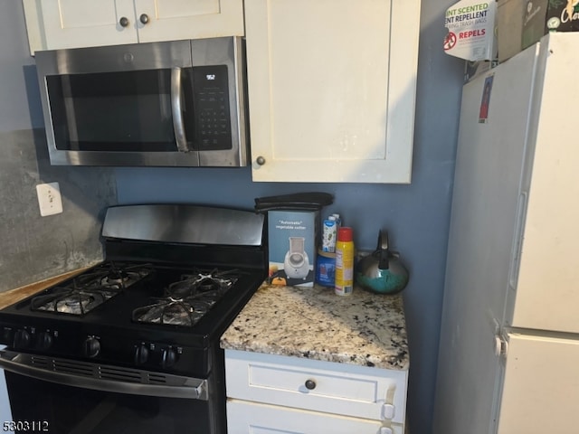 kitchen with white cabinetry, black range with gas stovetop, light stone countertops, and white fridge