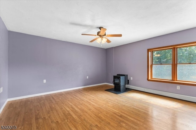 spare room with a baseboard radiator, a wood stove, light hardwood / wood-style floors, and ceiling fan