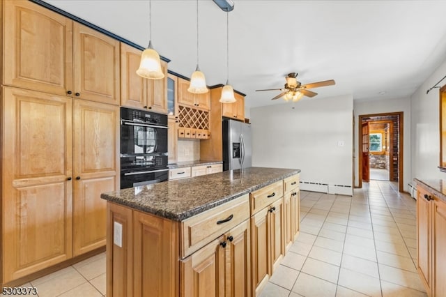 kitchen with ceiling fan, double oven, stainless steel refrigerator with ice dispenser, a center island, and dark stone countertops