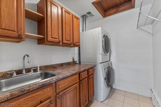 laundry room with cabinets, a baseboard heating unit, stacked washer / drying machine, light tile patterned flooring, and sink