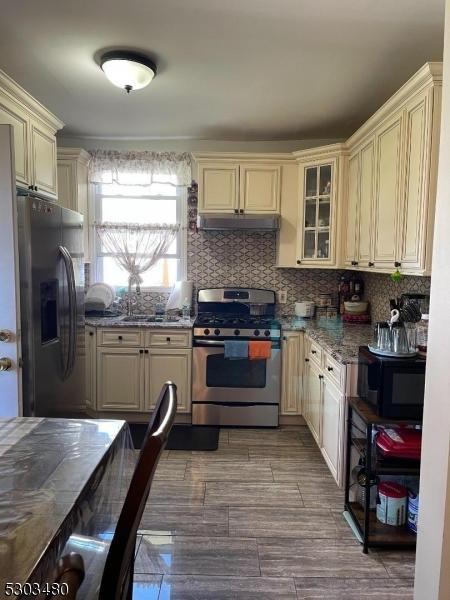 kitchen featuring stainless steel appliances, light stone countertops, backsplash, and cream cabinetry