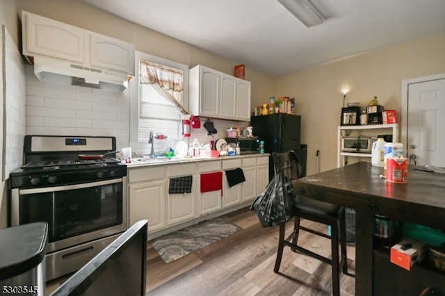 kitchen featuring wood-type flooring, stainless steel gas stove, white cabinets, sink, and black fridge