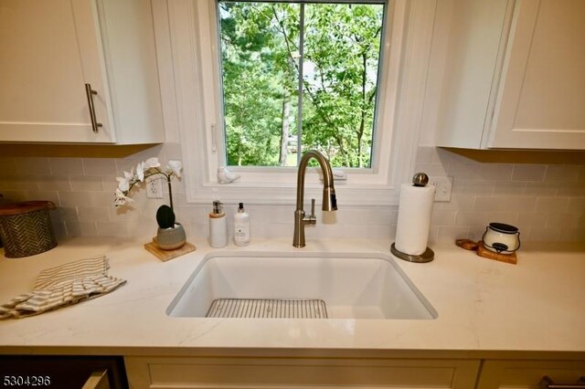 interior details featuring sink, light stone countertops, backsplash, and white cabinetry