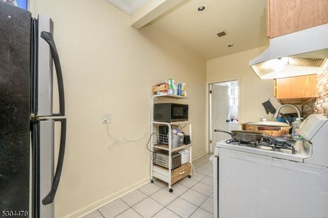 kitchen featuring black refrigerator, extractor fan, white range with gas cooktop, and light tile patterned flooring